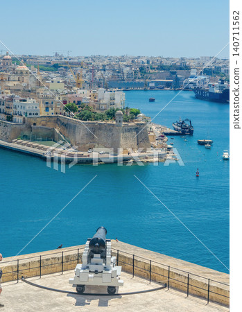 Historic cannon at Saluting Battery overlooking Grand Harbour Valletta Malta with Three Cities fortifications ships and blue sea Historic cannon at Saluting Battery overlooking Grand Harbour Valletta Malta with Three Cities fortifications ships and blue sea 140711562