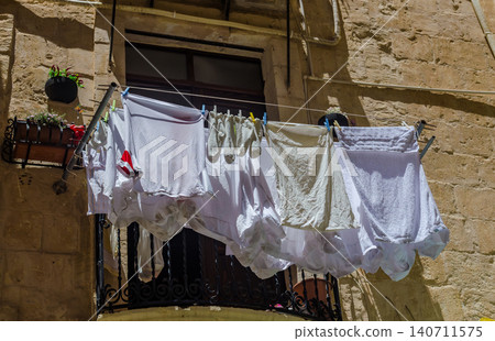 White laundry drying on clothesline on traditional iron balcony of old limestone house in sunny Mediterranean street in Malta 140711575