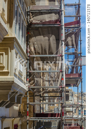 Metal scaffolding with protective net on facade of old limestone building under restoration on historic street in sunny Malta Metal scaffolding with protective net on facade of old limestone building under restoration on historic street in sunny Malta 140711578