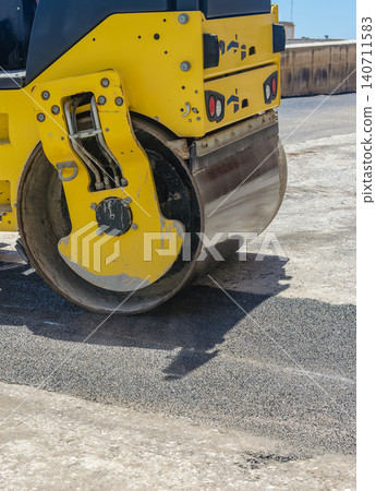 Yellow road roller compacting fresh asphalt on construction site close up of heavy machinery steamroller paving street in sunlight Yellow road roller compacting fresh asphalt on construction site close up of heavy machinery steamroller paving street in sunlight 140711583