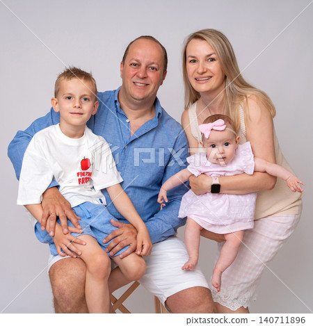 A beautiful blonde mother, a smiling father holding their infant daughter, and their young son posing together for a lovely family portrait in a bright, minimalist studio environment. High-quality A beautiful blonde mother, a smiling father holding their infant daughter, and their young son posing together for a lovely family portrait in a bright, minimalist studio environment. High-quality 140711896