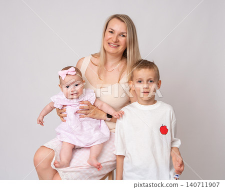 Close-up studio portrait of a radiant blonde mother, her preteen son, and her adorable infant daughter. All three are looking directly into the camera with bright, genuine smiles. Beautiful family of Close-up studio portrait of a radiant blonde mother, her preteen son, and her adorable infant daughter. All three are looking directly into the camera with bright, genuine smiles. Beautiful family of 140711907