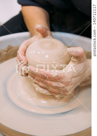 Ceramic clay. Pottery art. Unrecognizable experienced female hands forming raw using craft electric artisan wheel in master workplace. 140712117