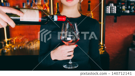 Red wine serving. Barman working. Unrecognizable bartender man hands pouring alcohol drink from bottle for woman bar customer. Red wine serving. Barman working. Unrecognizable bartender man hands pouring alcohol drink from bottle for woman bar customer. 140712141