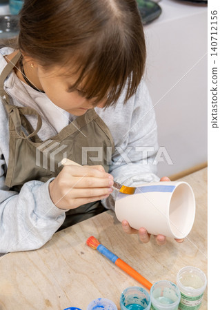 Coloring pottery. Handmade ceramic. Talented child painting on cup using brush developing art skill in artisan professional studio. Coloring pottery. Handmade ceramic. Talented child painting on cup using brush developing art skill in artisan professional studio. 140712156