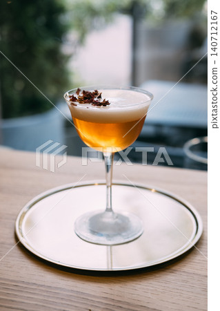Served drink. Bright beverage. Orange cocktail with frothy white top in stemmed glass. Refreshing mix with aroma flavor on outdoor bar table. Served drink. Bright beverage. Orange cocktail with frothy white top in stemmed glass. Refreshing mix with aroma flavor on outdoor bar table. 140712167