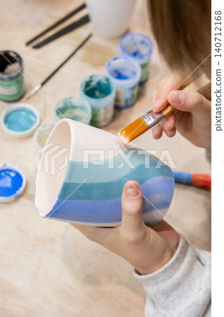 Ceramic art. Pottery class. Unrecognizable talented child hand painting on cup using brush developing creative skill in artisan workshop. Ceramic art. Pottery class. Unrecognizable talented child hand painting on cup using brush developing creative skill in artisan workshop. 140712168