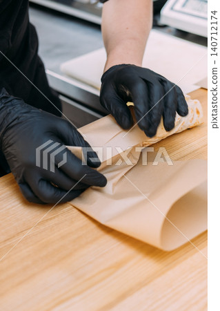Wrapping fast food. Preparing shawarma. Gloved chef hand packing meal in culinary paper on wooden table. Professional kitchen service. Wrapping fast food. Preparing shawarma. Gloved chef hand packing meal in culinary paper on wooden table. Professional kitchen service. 140712174
