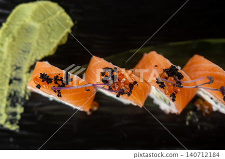 Salmon roll. Seafood dish. Row sushi with black caviar red ikura wasabi sauce on black. Oriental menu meal with herb sprouts. Salmon roll. Seafood dish. Row sushi with black caviar red ikura wasabi sauce on black. Oriental menu meal with herb sprouts. 140712184
