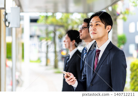 A man in a suit waiting for a bus at a bus stop. A man in a suit waiting for a bus at a bus stop. 140712211