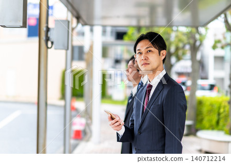 A man in a suit waiting for a bus at a bus stop. A man in a suit waiting for a bus at a bus stop. 140712214