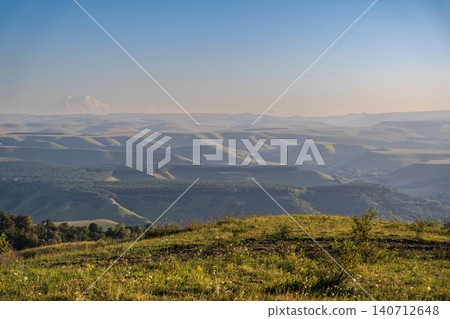 Panoramic view of the green valley and the snowy peak of Mount Elbrus on the horizon against the blue sky on a sunny clear morning in Kislovodsk Stavropol territory, Russia Panoramic view of the green valley and the snowy peak of Mount Elbrus on the horizon against the blue sky on a sunny clear morning in Kislovodsk Stavropol territory, Russia 140712648