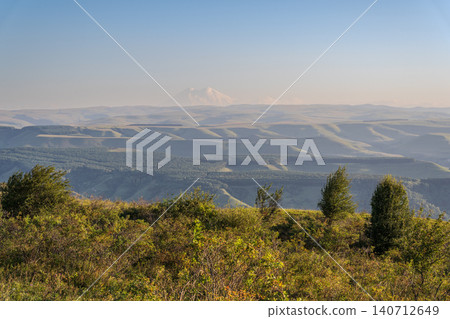 Panoramic view of the green valley and the snowy peak of Mount Elbrus on the horizon against the blue sky on a sunny clear morning in Kislovodsk Stavropol territory, Russia Panoramic view of the green valley and the snowy peak of Mount Elbrus on the horizon against the blue sky on a sunny clear morning in Kislovodsk Stavropol territory, Russia 140712649