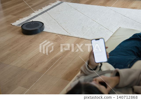 一位家庭主婦正躺在沙發上放鬆,旁邊放著一台掃地機器人。 一位家庭主婦正躺在沙發上放鬆,旁邊放著一台掃地機器人。 140712868