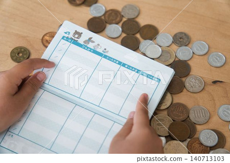 A child's hand opening a pocket money ledger and coins 140713103