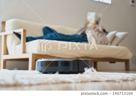 A person napping on the sofa with a robot vacuum cleaner. A person napping on the sofa with a robot vacuum cleaner. 140713104