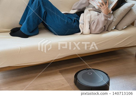 A person napping on the sofa with a robot vacuum cleaner. A person napping on the sofa with a robot vacuum cleaner. 140713106