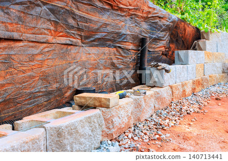 Cement blocks are laid out along dirt path with tools nearby at construction site during retaining wall install Cement blocks are laid out along dirt path with tools nearby at construction site during retaining wall install 140713441