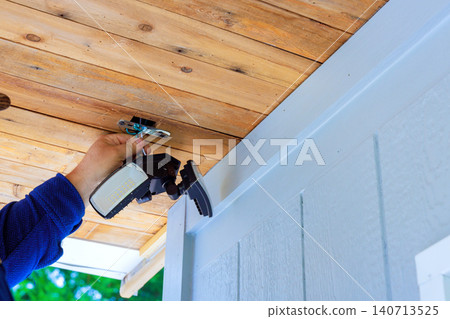 Hand holds light fixture while it is being installed on wooden ceiling outside house in garden. 140713525