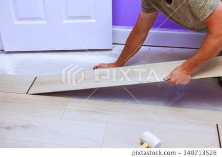 Carpenter works on laying new flooring in room with tools project takes place indoors. 140713526