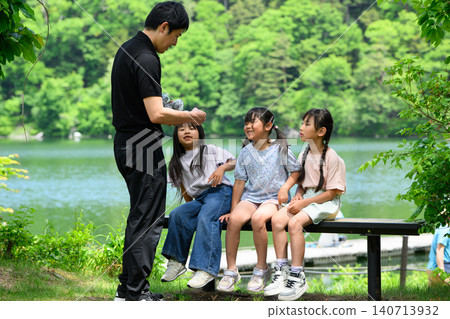 小學生們在湖邊長椅上休息時,從老師那裡領取了講義,周圍綠樹環繞。 小學生們在湖邊長椅上休息時,從老師那裡領取了講義,周圍綠樹環繞。 140713932