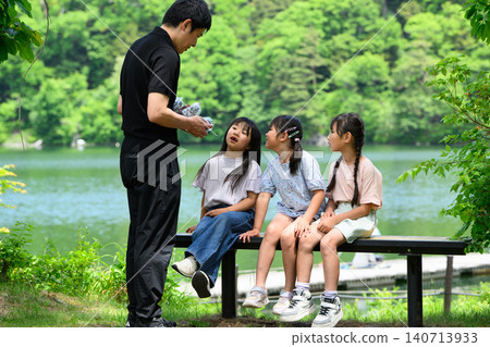 小學生們在湖邊長椅上休息時,從老師那裡領取了講義,周圍綠樹環繞。 小學生們在湖邊長椅上休息時,從老師那裡領取了講義,周圍綠樹環繞。 140713933