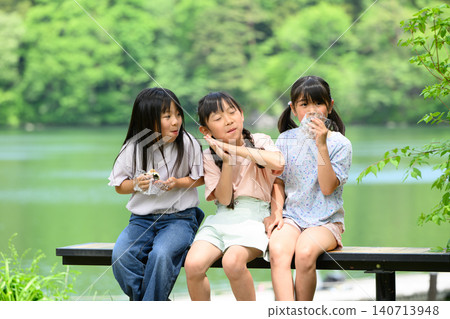 一群小學生在湖邊長椅上,被綠樹環繞,開心地一起吃著飯糰。 一群小學生在湖邊長椅上,被綠樹環繞,開心地一起吃著飯糰。 140713948
