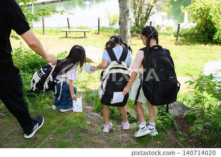 小學生女生們看著地圖,找到一條路線,並在鬱鬱蔥蔥的自然綠植中指出來。 小學生女生們看著地圖,找到一條路線,並在鬱鬱蔥蔥的自然綠植中指出來。 140714020