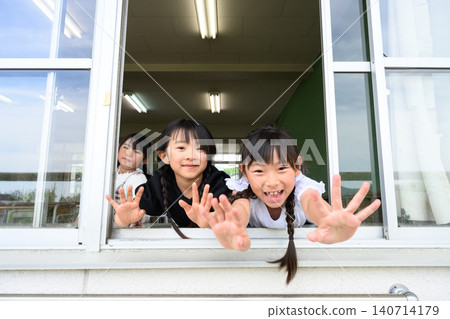 A female elementary school student opens the classroom window and waves with a smile towards the outside. A female elementary school student opens the classroom window and waves with a smile towards the outside. 140714179