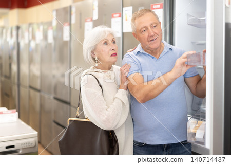 Elderly couple stands in a hardware store and chooses a refrigerator Elderly couple stands in a hardware store and chooses a refrigerator 140714487