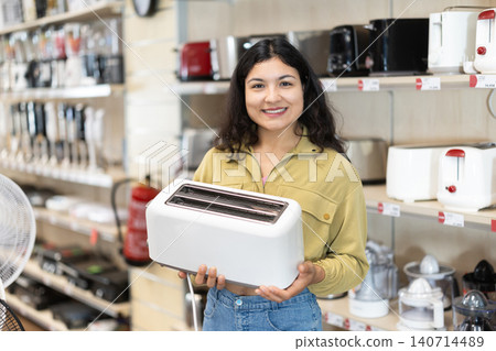 Positive woman choosing toaster in hypermarket and smiling Positive woman choosing toaster in hypermarket and smiling 140714489