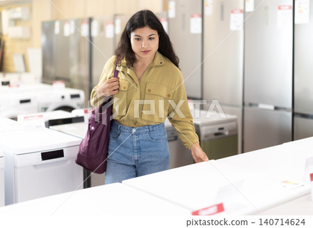 Woman is shopping in a store - choosing washing machine Woman is shopping in a store - choosing washing machine 140714624