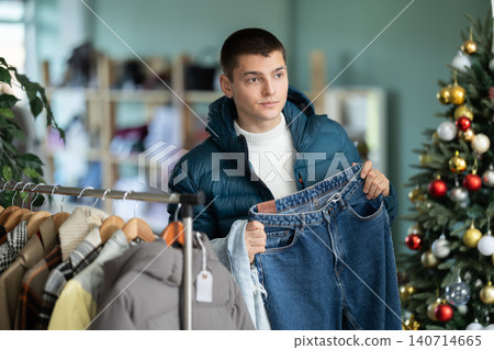 Guy client pre-examine fabric and style of product, is busy choosing jeans, X mas discount. Guy client pre-examine fabric and style of product, is busy choosing jeans, X mas discount. 140714665