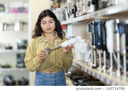 Young woman choosing electric hand blender at household appliances store 140714766