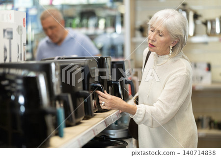 Elderly woman choosing air fryer at household appliances store Elderly woman choosing air fryer at household appliances store 140714838