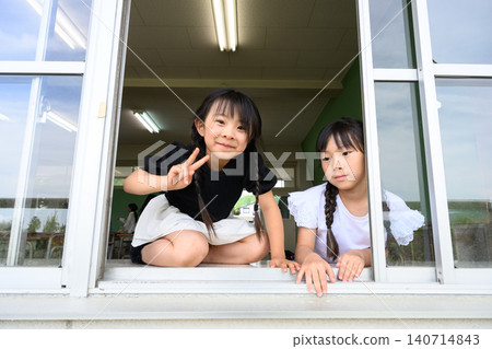 A female elementary school student opens the classroom window and waves with a smile towards the outside. A female elementary school student opens the classroom window and waves with a smile towards the outside. 140714843