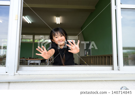 A female elementary school student opens the classroom window and waves with a smile towards the outside. A female elementary school student opens the classroom window and waves with a smile towards the outside. 140714845