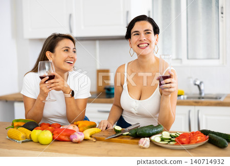 Two cheerful female roommates drinking wine and preparing dinner at home Two cheerful female roommates drinking wine and preparing dinner at home 140714932