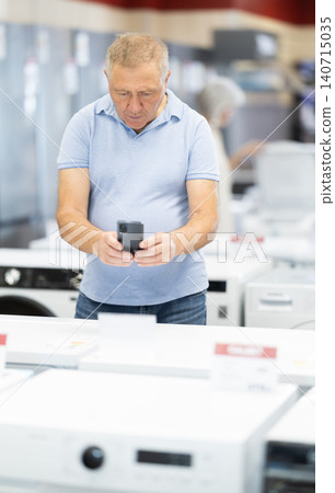 Elderly man scanning QR-code on washing machine at household appliances store Elderly man scanning QR-code on washing machine at household appliances store 140715035