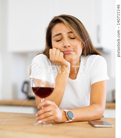 Young depressed Latina with glass of wine and silent phone in kitchen Young depressed Latina with glass of wine and silent phone in kitchen 140715146