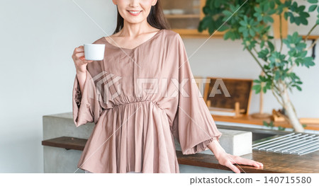 Middle-aged Asian woman drinking coffee/tea in kitchen/dining room Middle-aged Asian woman drinking coffee/tea in kitchen/dining room 140715580
