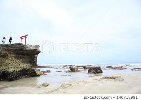 A red torii gate amidst waves crashing on the sandy beach and rocky outcrops. A red torii gate amidst waves crashing on the sandy beach and rocky outcrops. 140715981