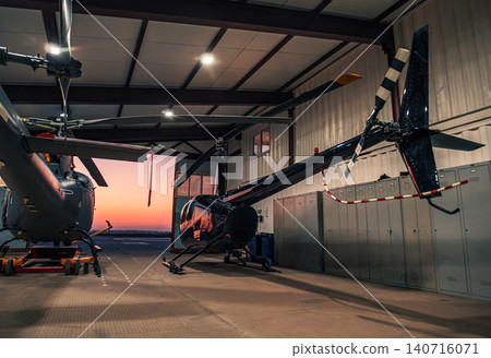 Helicopters parked in a hangar at sunset. 140716071