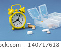Yellow alarm clock with scattered pills and pill box on blue background, time to take medicine concept 140717618