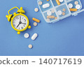 Pills and supplement with yellow alarm clock and medication pill box on blue background, top view 140717619