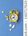 Alarm clock with medicine pills and vitamin capsule on blue background, top view 140717620