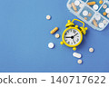 Medicine pills, tablets and capsules with yellow alarm clock and pill box on blue background, top view 140717622