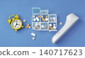 Medical pills organizer, yellow alarm clock, and digital thermometer on blue background 140717623