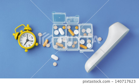 Medical pills organizer, yellow alarm clock, and digital thermometer on blue background Medical pills organizer, yellow alarm clock, and digital thermometer on blue background 140717623