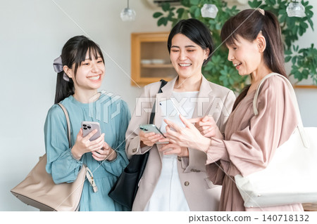 Businesswomen (colleagues, boss, subordinates) talking while looking at smartphones Businesswomen (colleagues, boss, subordinates) talking while looking at smartphones 140718132